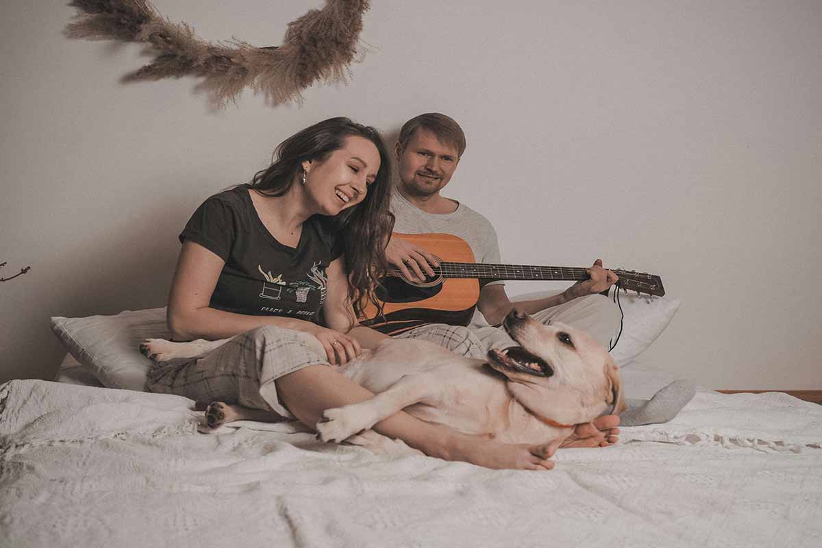 dog man, and woman sing a song with a giter on the bed in the room.